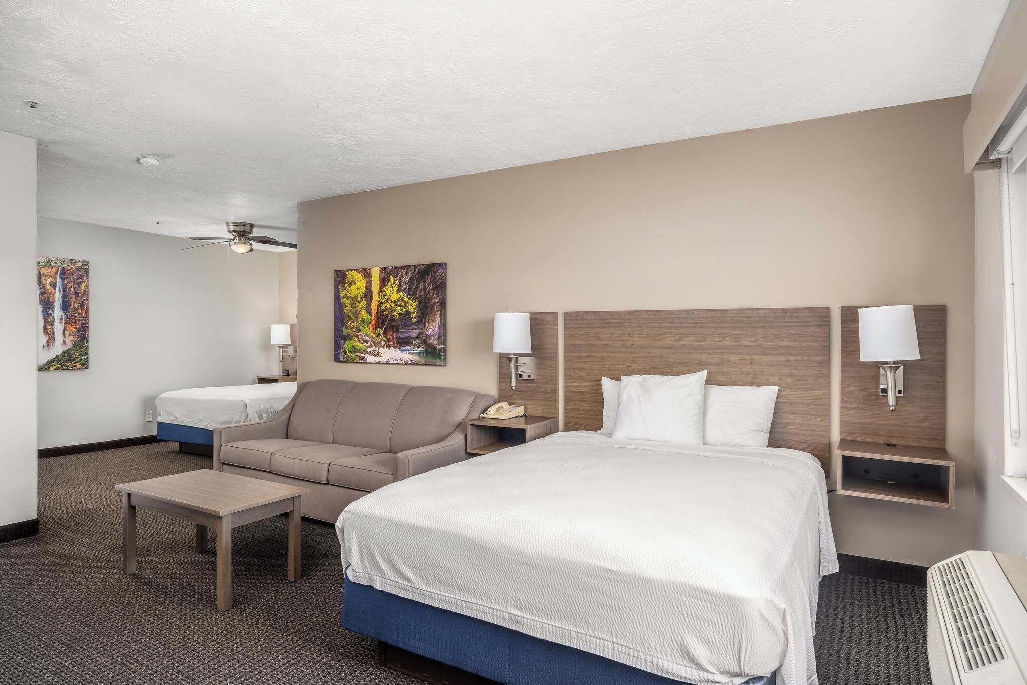 Une chambre d’hôtel avec un grand lit, un canapé, une petite table et deux lampes fixées au mur.