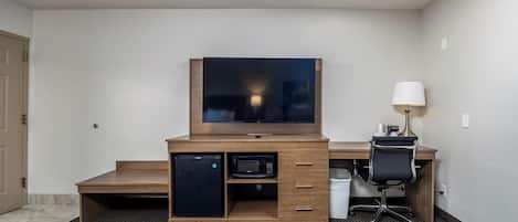 Une chambre d’hôtel équipée d’un bureau en bois, d’une télévision, d’un four à micro-ondes, d’un réfrigérateur, d’une chaise et d’une lampe.