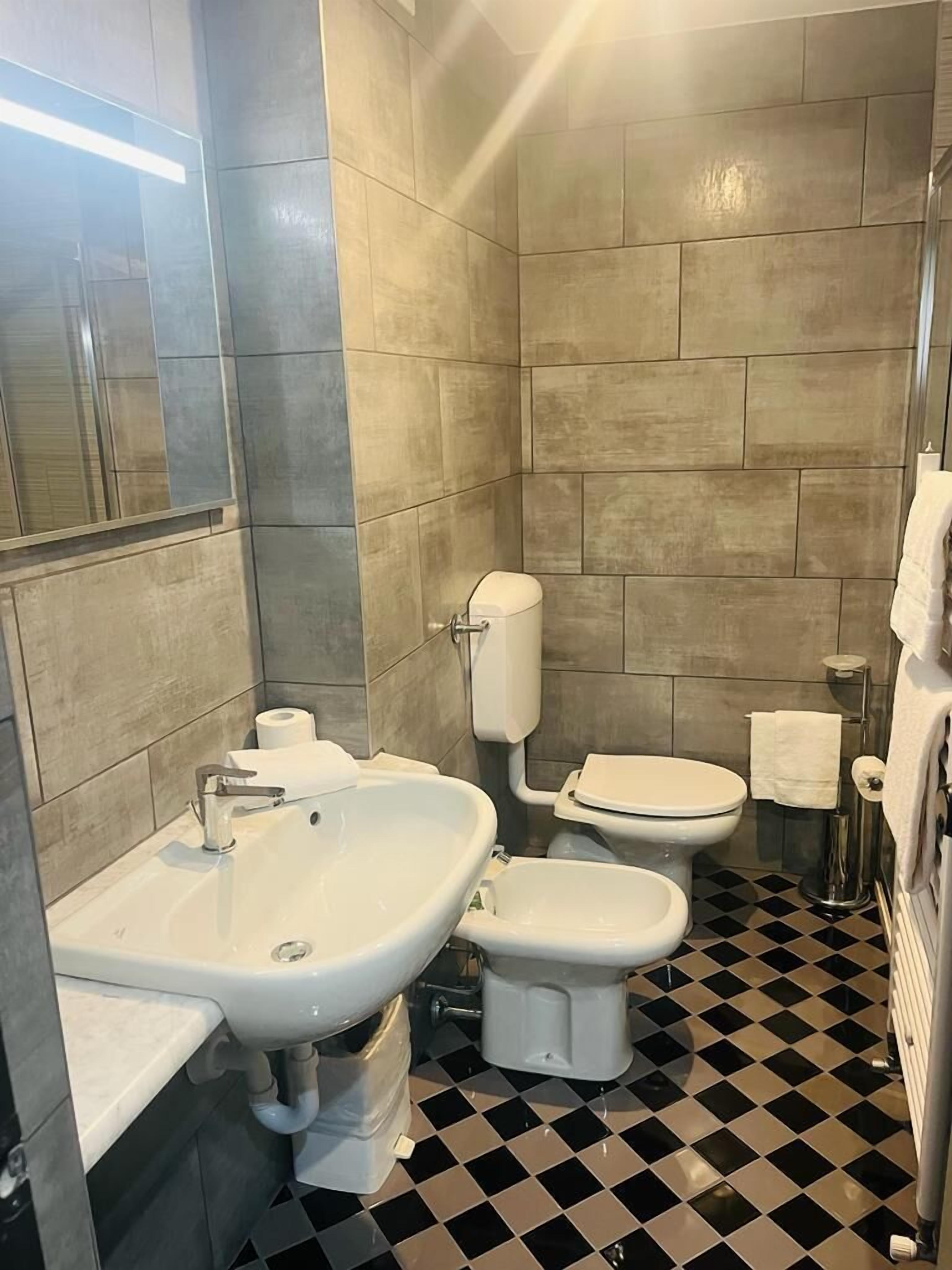 A bathroom with a sink, toilet, and bidet. The floor has a black and white checkered pattern.