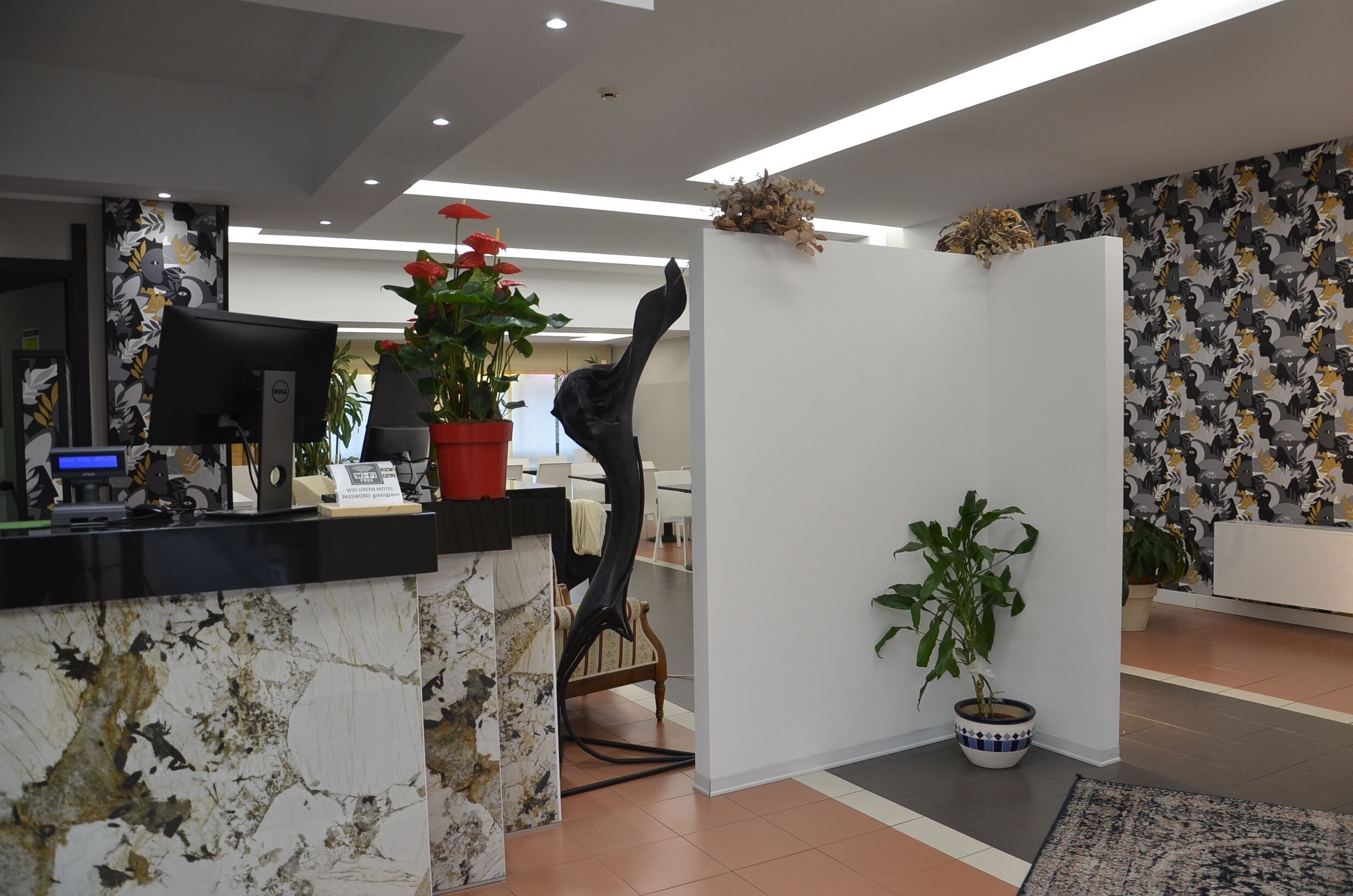 A reception area with a marble counter, a computer, a potted plant, and a decorative sculpture.