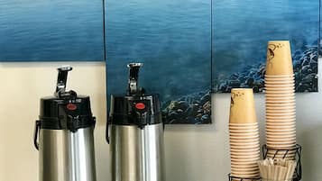 Deux thermos en acier inoxydable, un petit récipient blanc et une pile de gobelets en bambou sont posés sur un comptoir, avec en arrière-plan une vue panoramique sur l’océan.