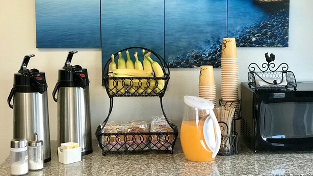 A kitchen counter with a coffee maker, thermos, bananas, bread, and a juice pitcher. - Sea-Tac Airport Value Inn (Des Moines)