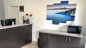A modern kitchen with dark cabinetry, a granite countertop, a microwave, and a cityscape painting. - Sea-Tac Airport Value Inn (Des Moines)