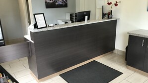 A reception desk with a cityscape painting, a framed certificate, and a desk lamp. - Sea-Tac Airport Value Inn (Des Moines)