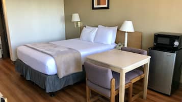 Quarto de hotel com cama, escrivaninha, cadeira, micro-ondas e telefone.