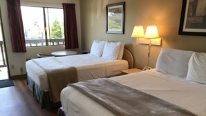 A hotel room with two beds, a small table, a chair, a lamp, and a window with curtains. - Sea-Tac Airport Value Inn (Des Moines)