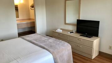 A hotel room with a bed, a television on a dresser, a mirror, and a bathroom visible in the background.