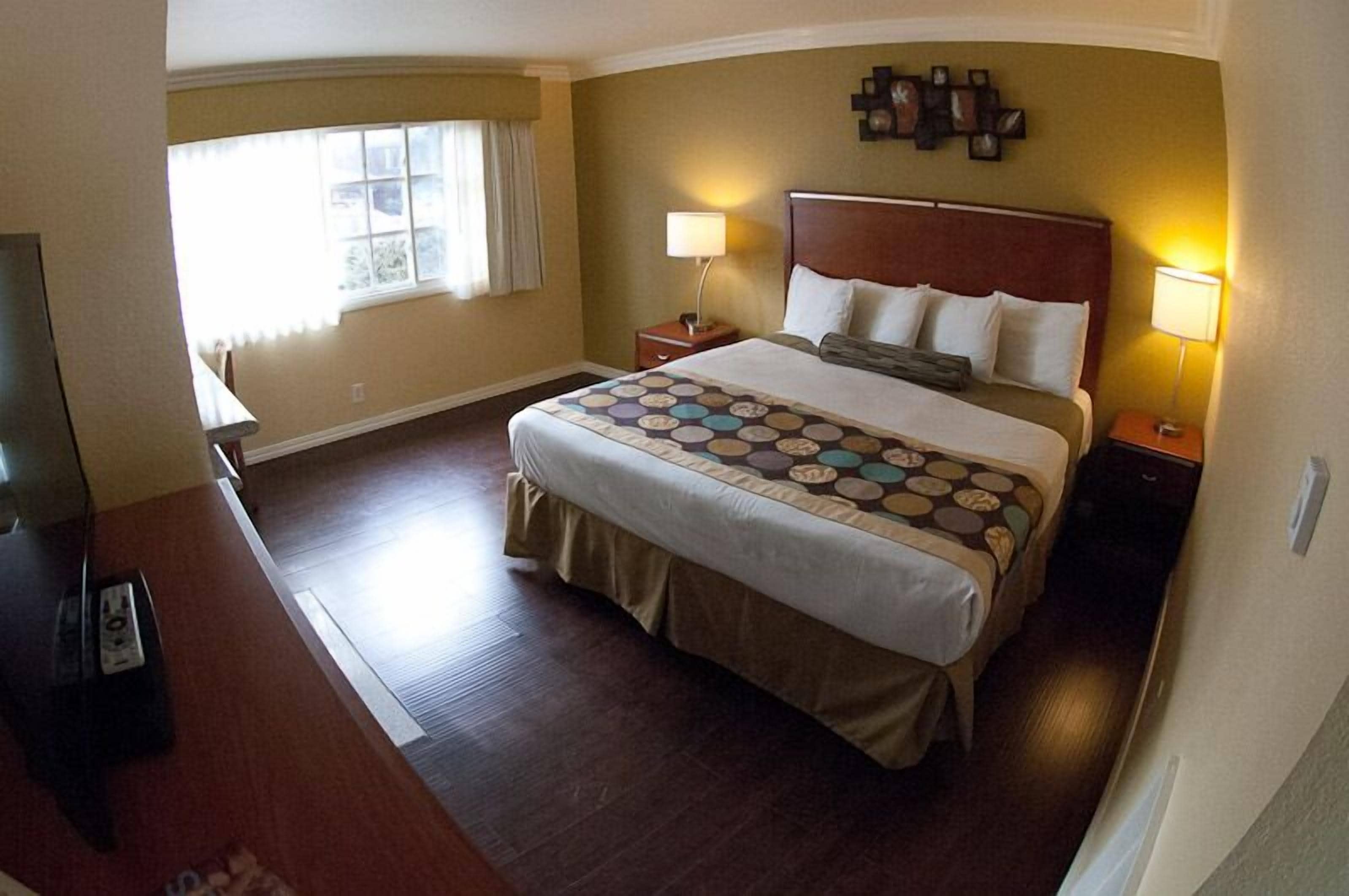 Una habitación de hotel con una cama grande, dos mesitas de noche con lámparas, un televisor y una ventana con cortinas.