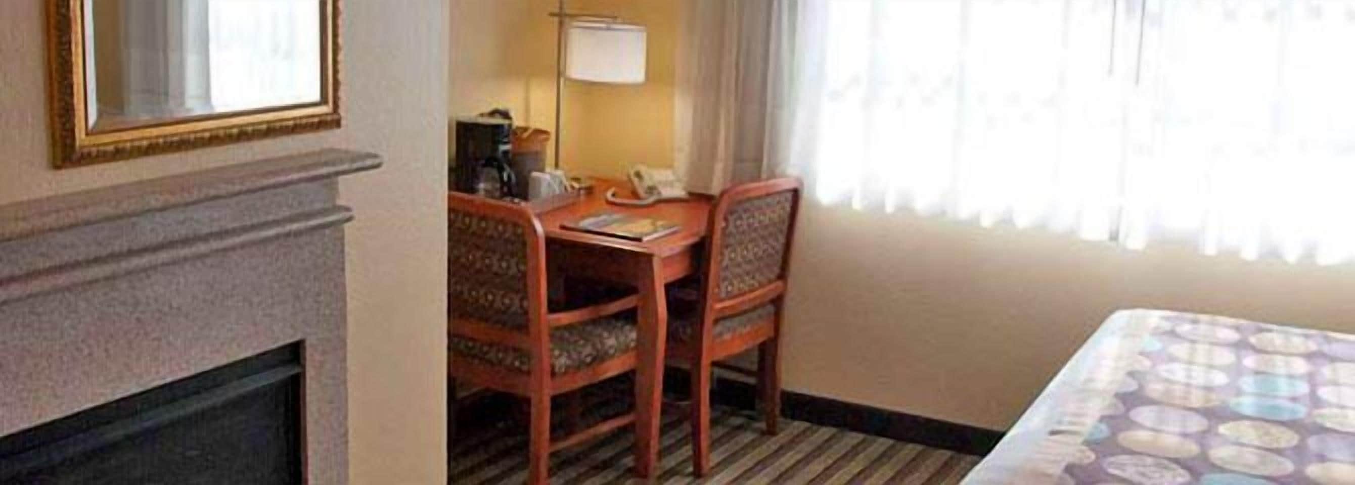 A hotel room with a bed, a desk with a chair, a telephone, and a window with curtains.