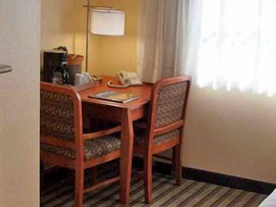 A hotel room with a bed, a desk with a chair, a telephone, and a window with curtains.