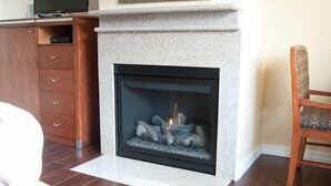 A modern fireplace with a stone surround, a wooden cabinet to the left, and a chair to the right. - Deer Haven Inn (Pacific Grove)