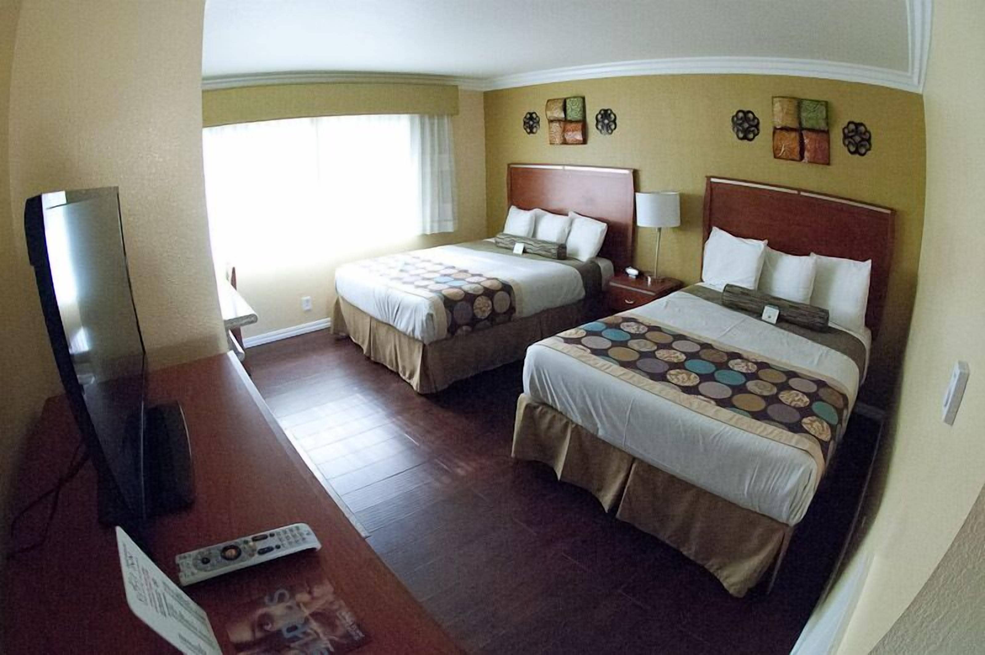 A hotel room with two beds, a TV, and a desk.