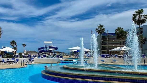 A swimming pool with a central fountain, surrounded by lounge chairs and umbrellas. - Port Royal Ocean Resort & Conference Center (Port Aransas)