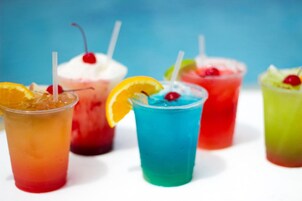 A variety of colorful drinks with straws and garnishes, including a blue drink with an orange slice and a cherry.