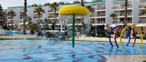 Parque acuático con una fuente grande, palmeras y una piscina con diseño de mosaico azul.