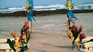 A beach ceremony setup with a wooden arch and floral decorations. - Port Royal Ocean Resort & Conference Center (Port Aransas)