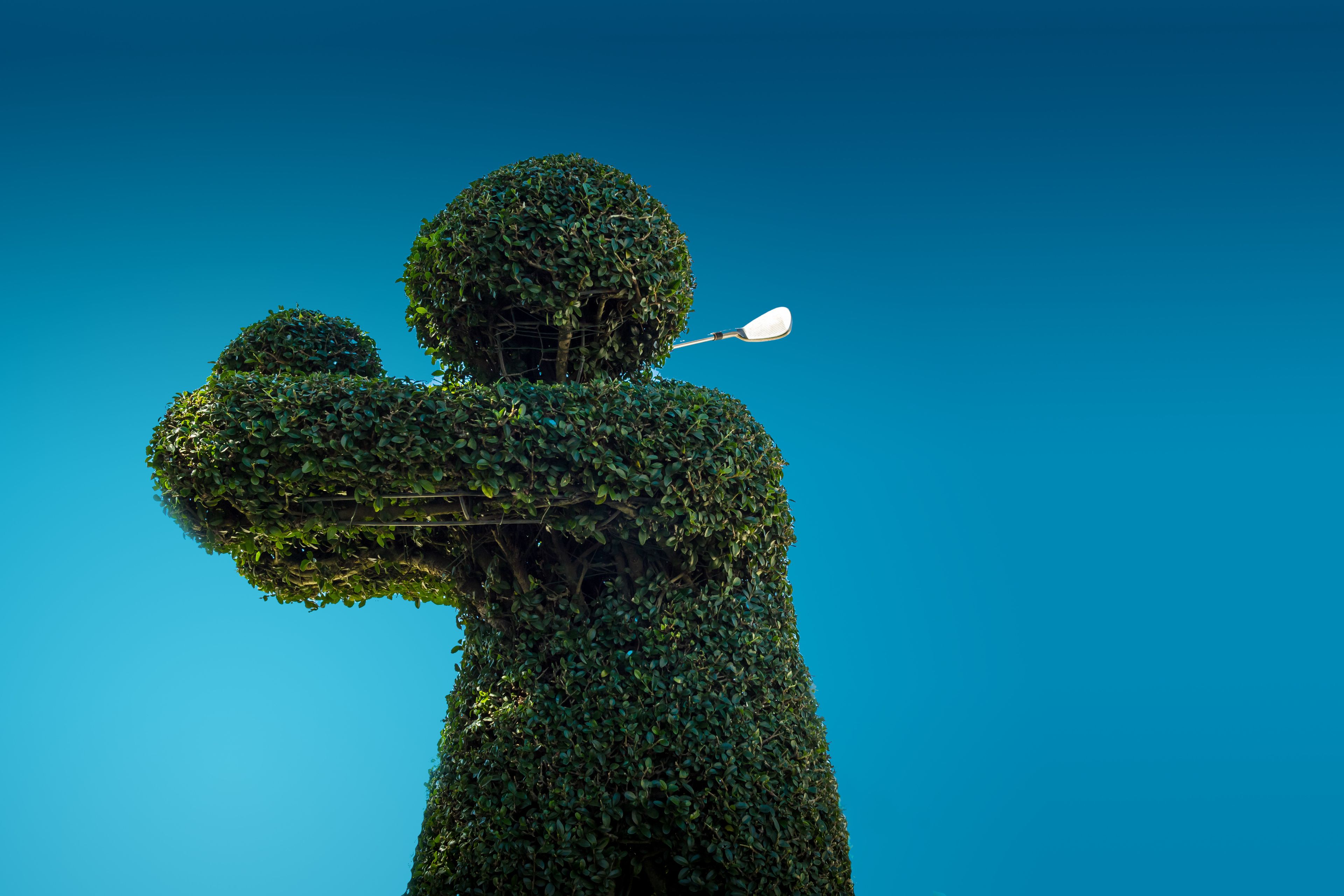 Une sculpture de jardin, représentant une personne les bras tendus, se détachant sur un ciel bleu clair.