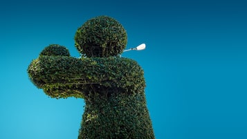Une sculpture de jardin, représentant une personne les bras tendus, se détachant sur un ciel bleu clair.