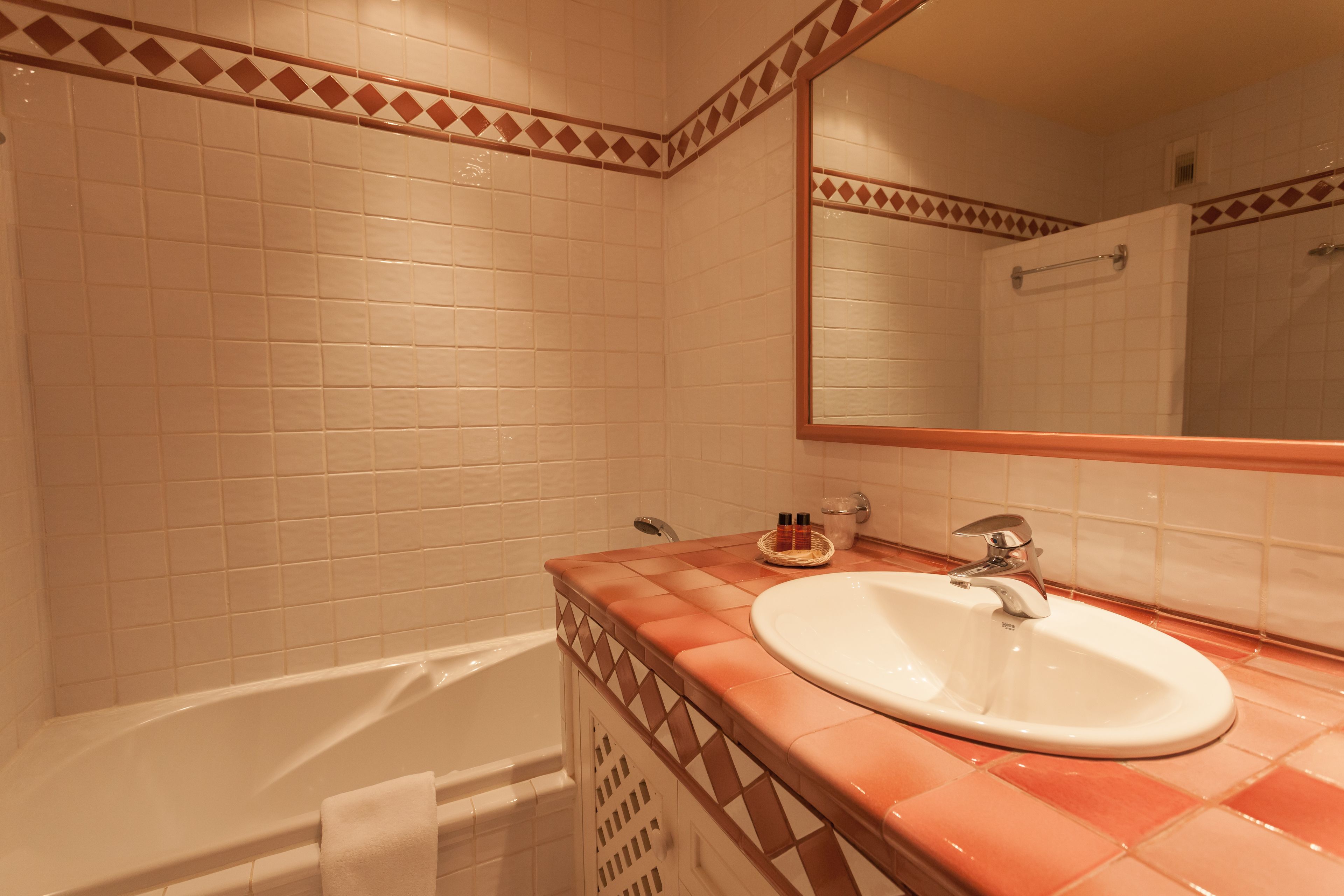 A bathroom with white tiles, a bathtub, a sink with a mirror, and a towel rack.