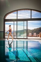 Piscina com água cristalina, uma pessoa de fato de banho e uma varanda com cadeiras e vista para a paisagem.