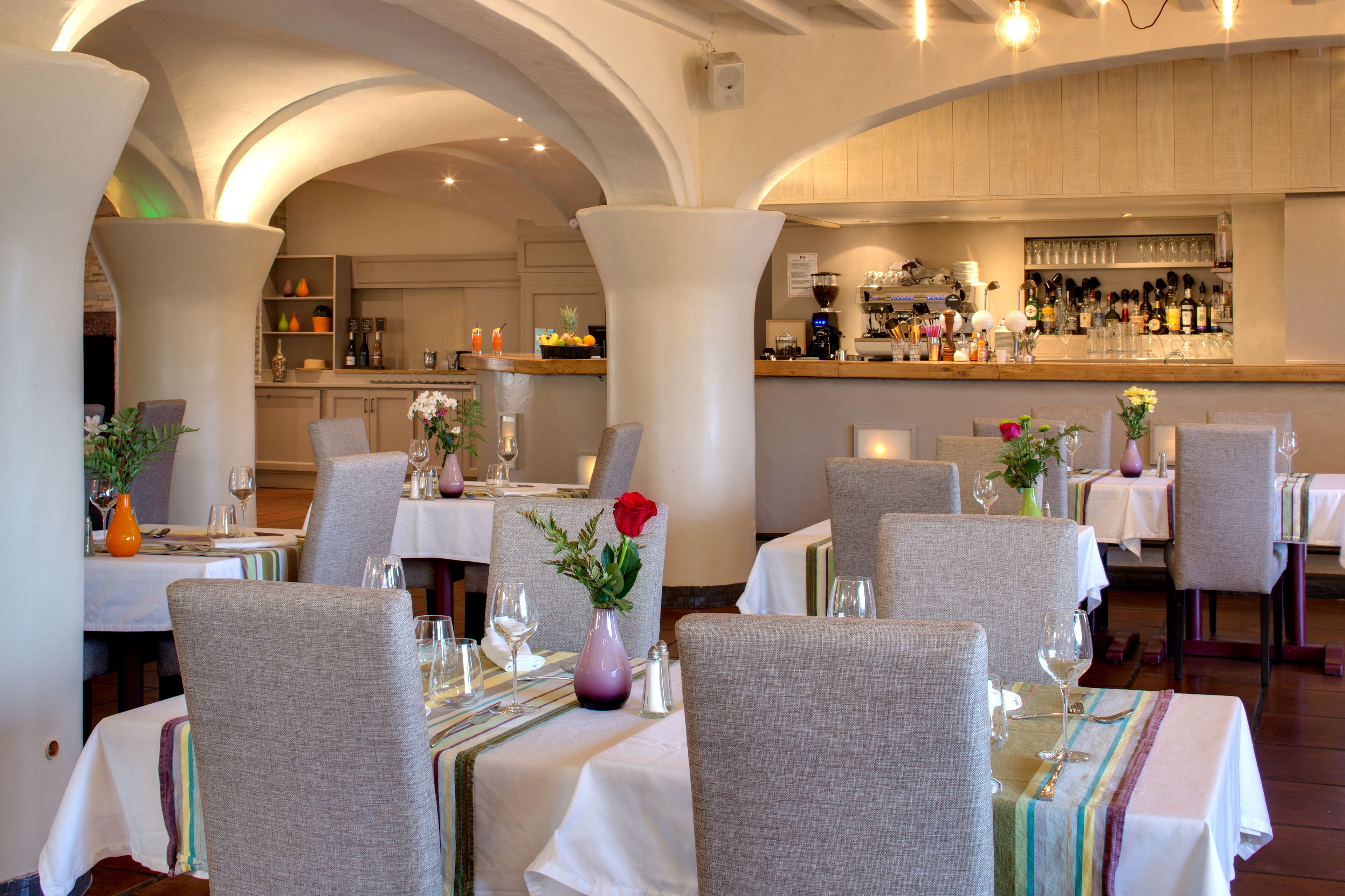 A restaurant with tables set for dining, a bar area, and a kitchen in the background.
