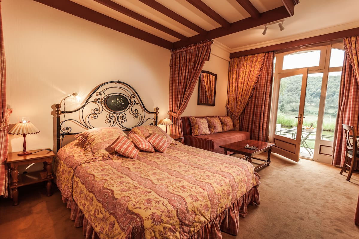 A bedroom with a large bed, a wooden bench, a nightstand, and a window with curtains.