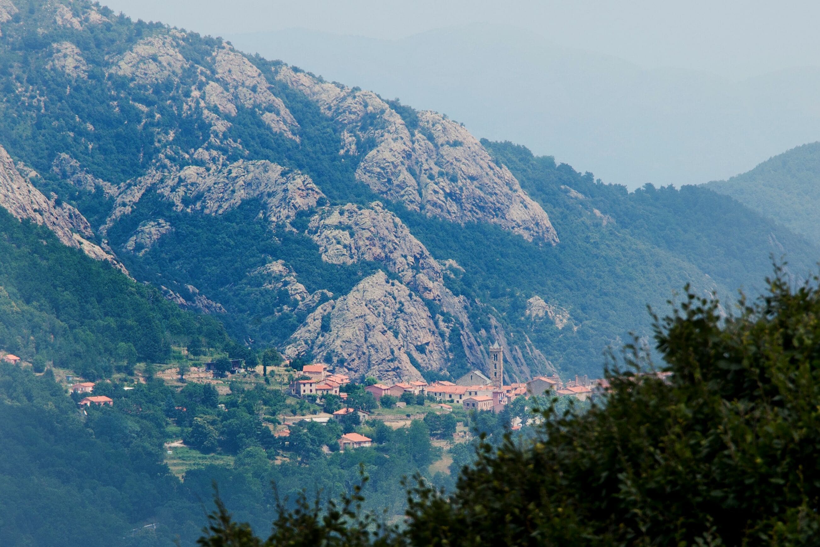 A mountainous landscape with a village nestled at its base, featuring traditional architecture and rocky terrain.
