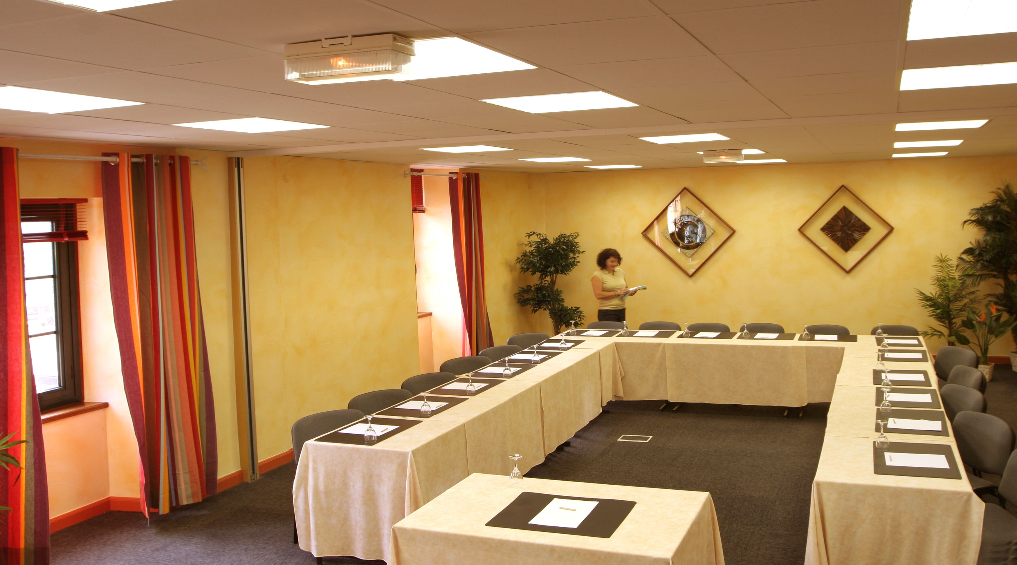 Un salón de conferencias con una larga mesa, sillas y un proyector en el techo.