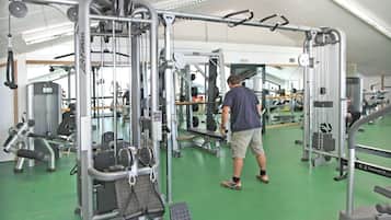 Une salle de sport équipée de divers appareils d’exercice, un homme utilisant un appareil à câbles et un sol vert.