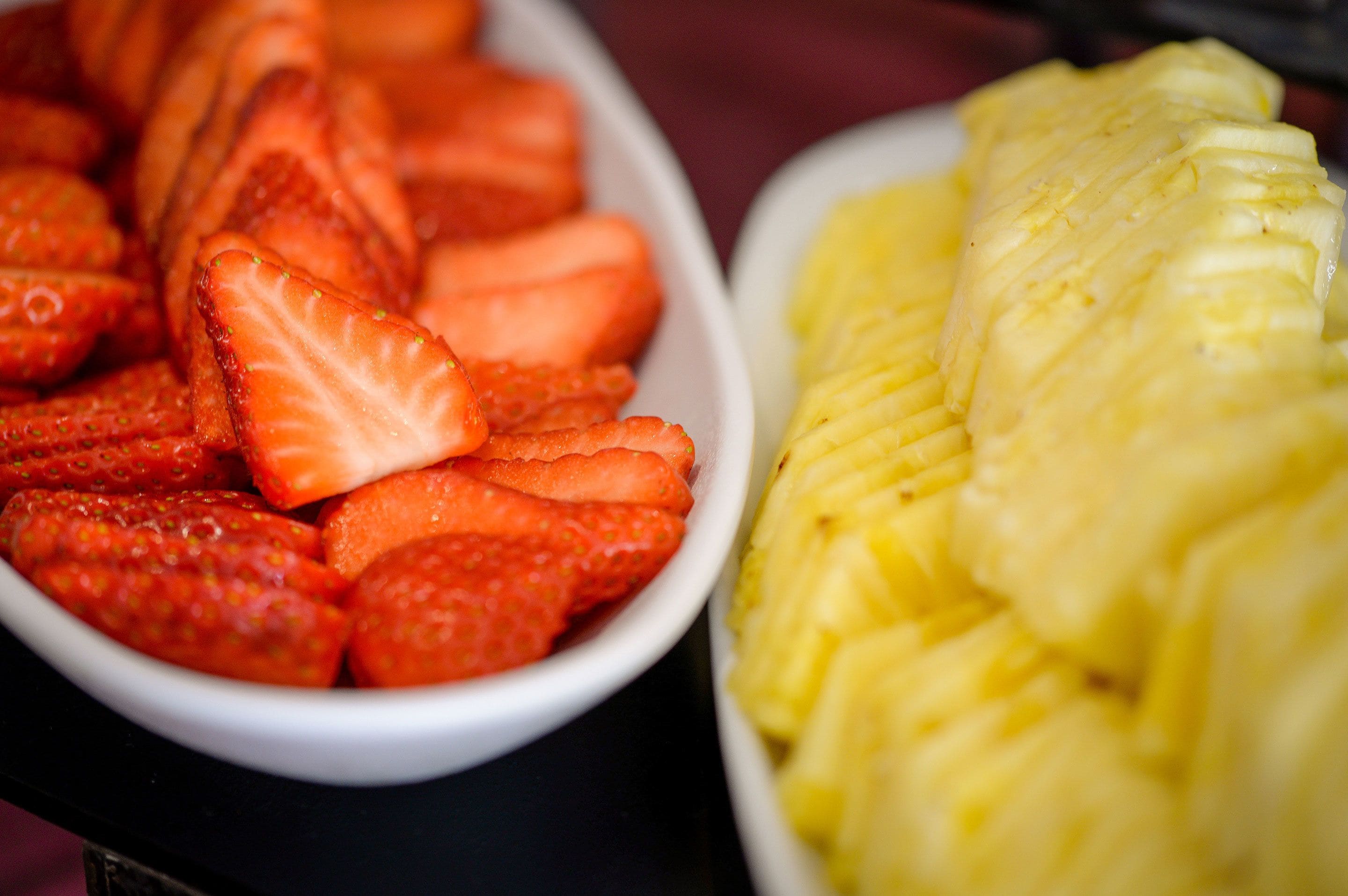 Dos tazones de fruta cortada, uno con fresas y el otro con piña.