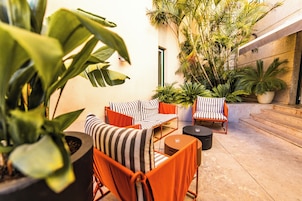 A well-lit outdoor seating area with striped chairs and a round table, surrounded by potted plants and a building entrance.