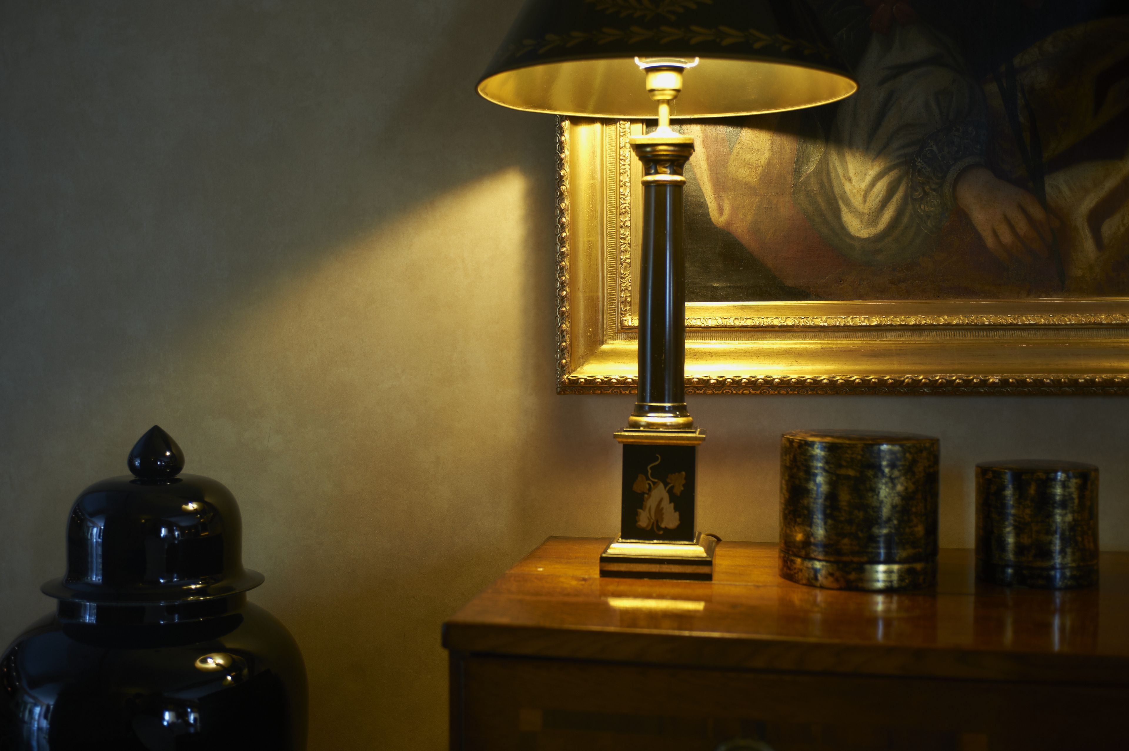 A lamp on a wooden table with a framed painting in the background.
