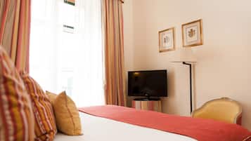 Habitación de hotel con cama, televisor sobre un soporte, una silla y dos cuadros en la pared.