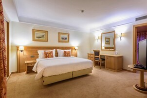 A hotel room with a large bed, bedside tables, a desk with a chair, a mirror, and two framed pictures on the wall.
