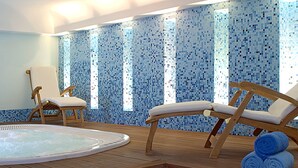 Et spa-område med et boblebad, to træloungestole og en flisevæg med et blåt mosaikmønster.