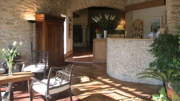 A stone-walled interior with a wooden table and chairs, a potted plant, and a stone counter with a lamp. - Auberge de Tavel (Tavel)
