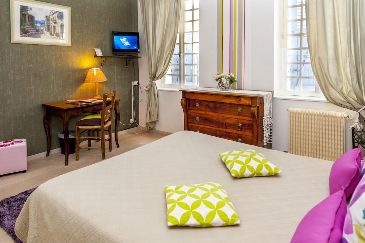 A hotel room with a bed, a desk, a chair, a dresser, a television, and a window with curtains.