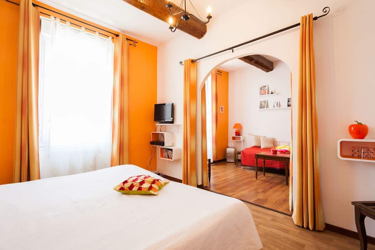 A hotel room with a bed, a television, a desk, and a chair. There is a door leading to another room.