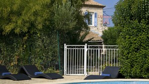 A pool area with lounge chairs, a gated entrance, and a building with a sign in the background. - Auberge de Tavel (Tavel)
