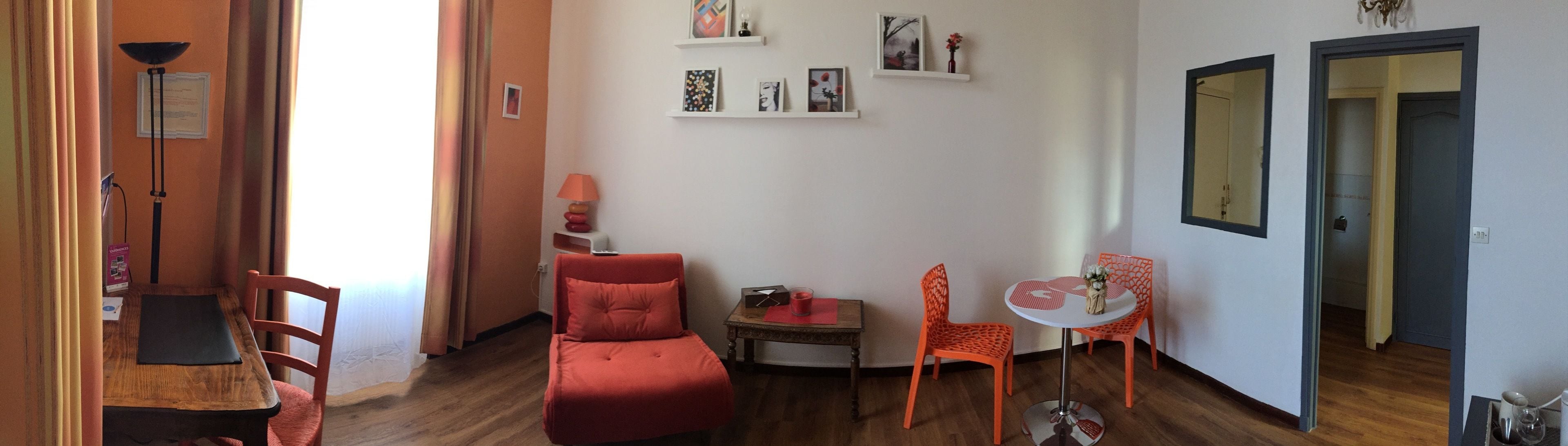 Un espacio habitable compacto con suelo de madera, un sofá rojo, una pequeña mesa con una vela y sillas naranjas.