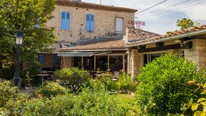 A stone building with a tiled roof, a covered patio with outdoor seating, and a sign indicating a business. - Auberge de Tavel (Tavel)