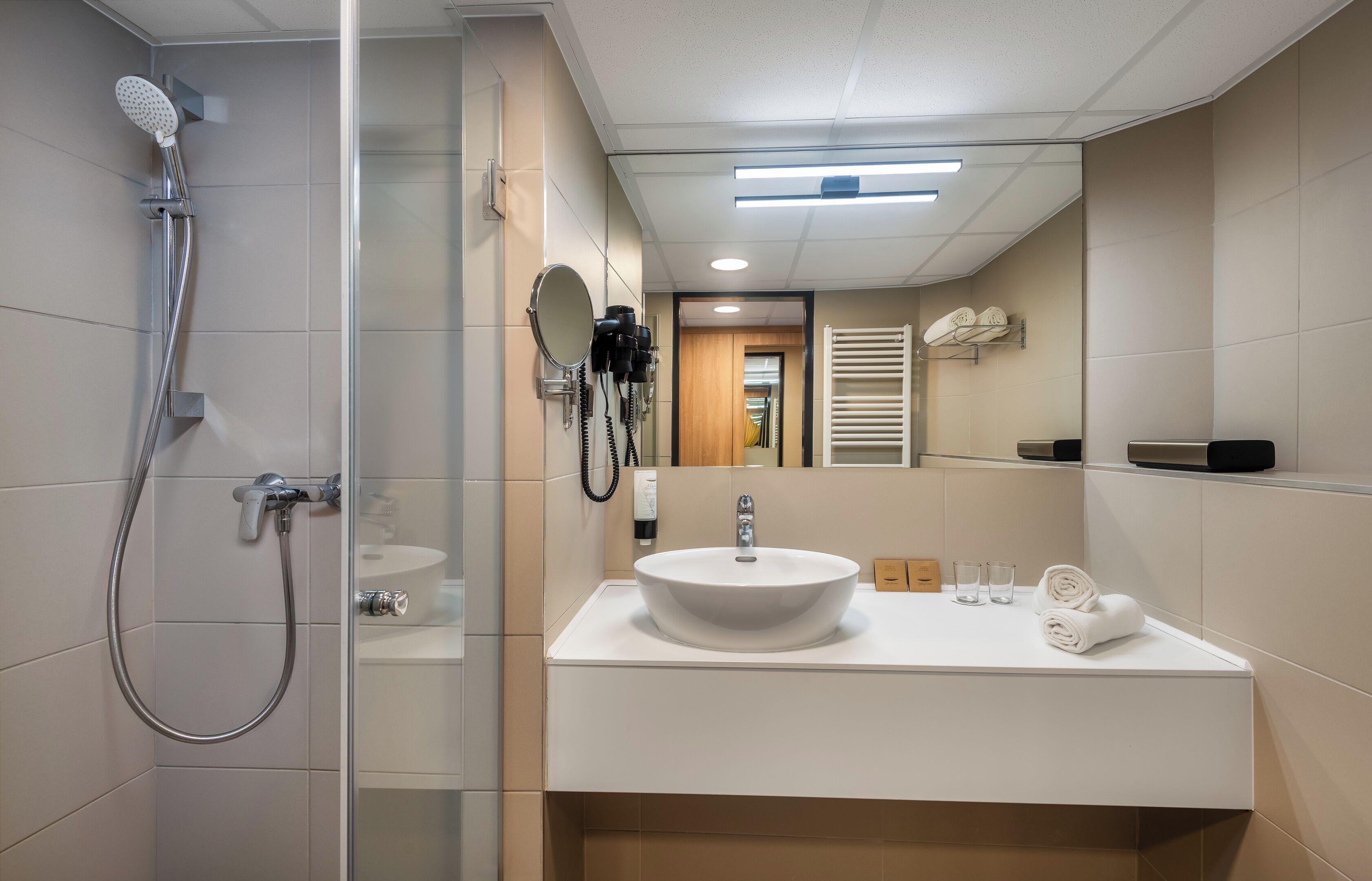 Un baño moderno con cabina de ducha de vidrio, lavamanos blanco, espejo y toallero.