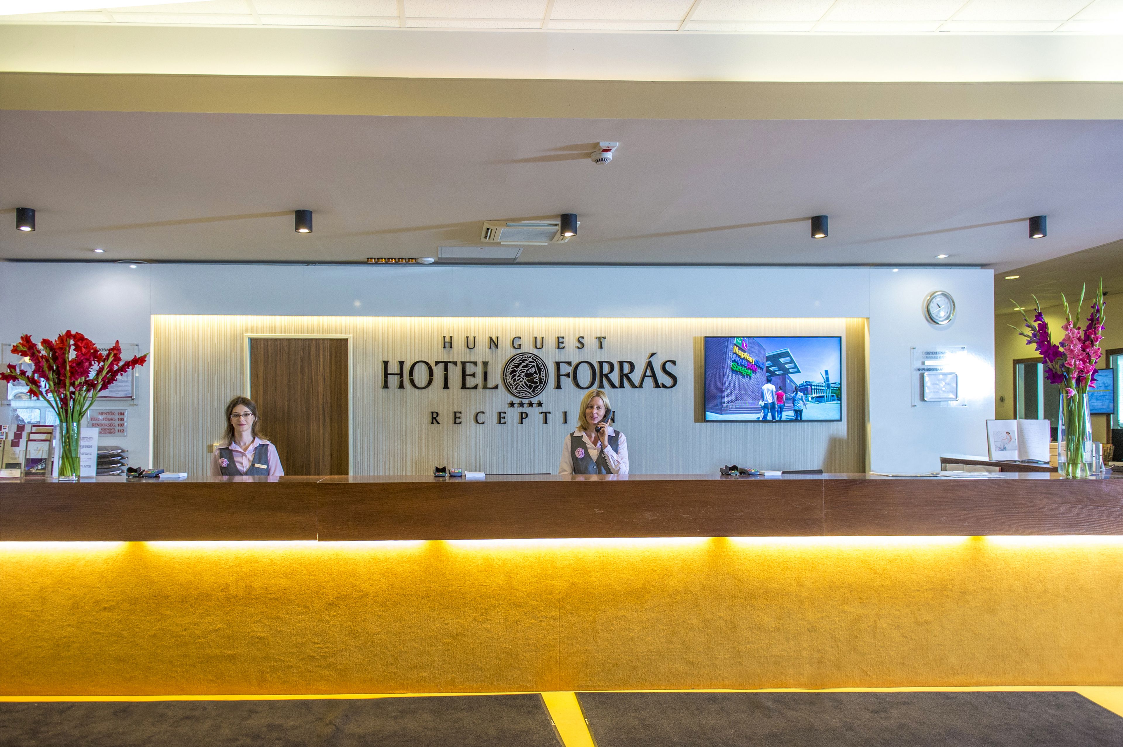 Una recepción de hotel de diseño moderno, con un reloj y una pantalla de televisión que muestra una imagen.