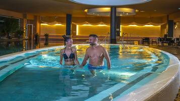 Una pareja en una piscina interior climatizada con un diseño de interiores moderno, que incluye una zona de estar y una escalera.