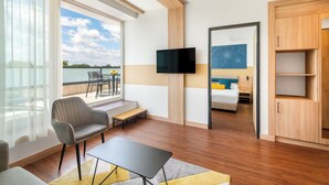 A hotel room with a balcony, a TV mounted on the wall, a bed with a blue headboard, and a wooden wardrobe. - Hunguest Szeged - ex Forrás (Szeged)