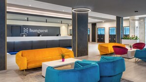 A modern hotel lobby with a reception desk, colorful seating, and large windows. - Hunguest Szeged - ex Forrás (Szeged)