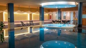 A modern indoor pool area with a central circular pool, seating around the perimeter, and a reception desk in the background. - Hunguest Szeged - ex Forrás (Szeged)
