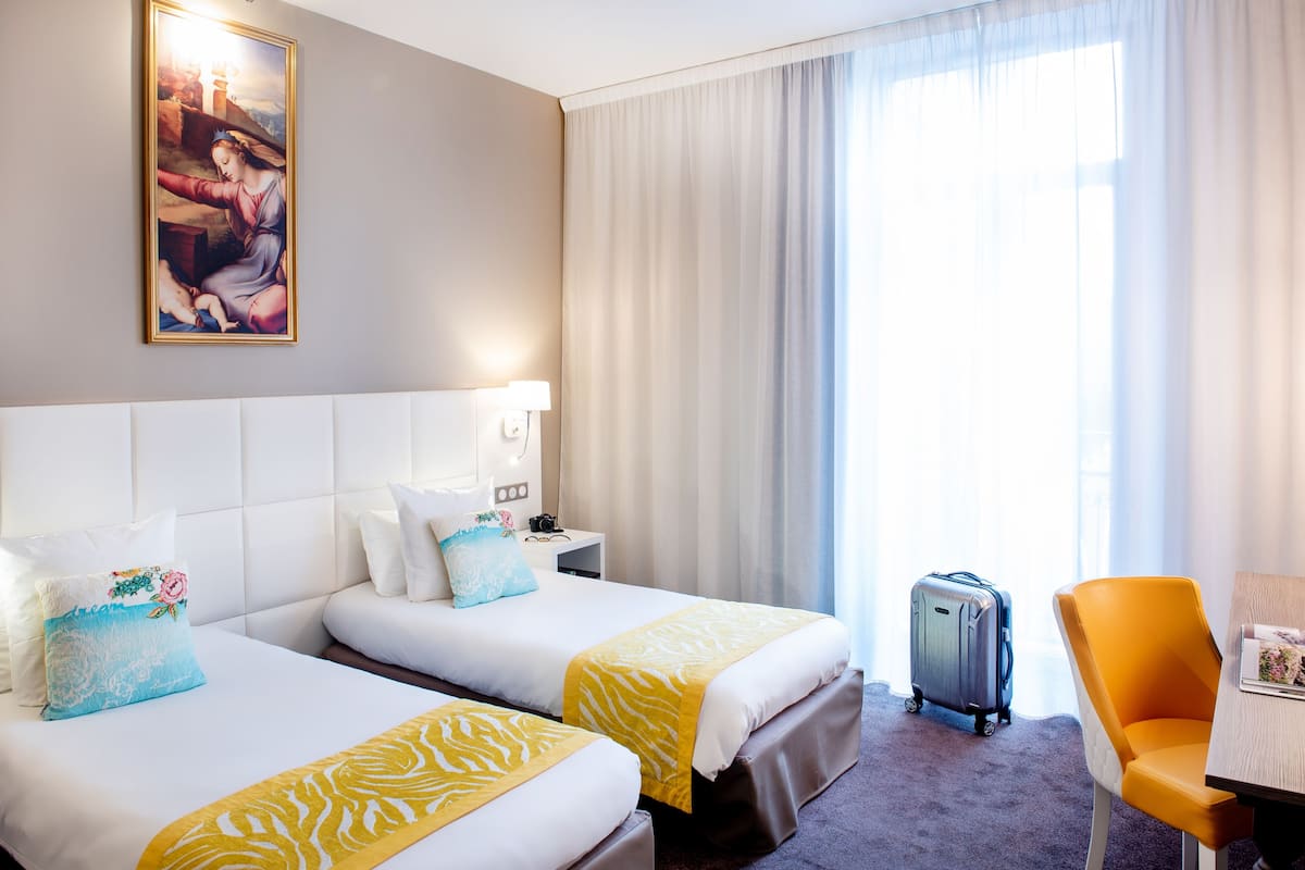 Ein Hotelzimmer mit zwei Betten, einem Schreibtisch, einem Stuhl, einem Koffer und einem Bild an der Wand.