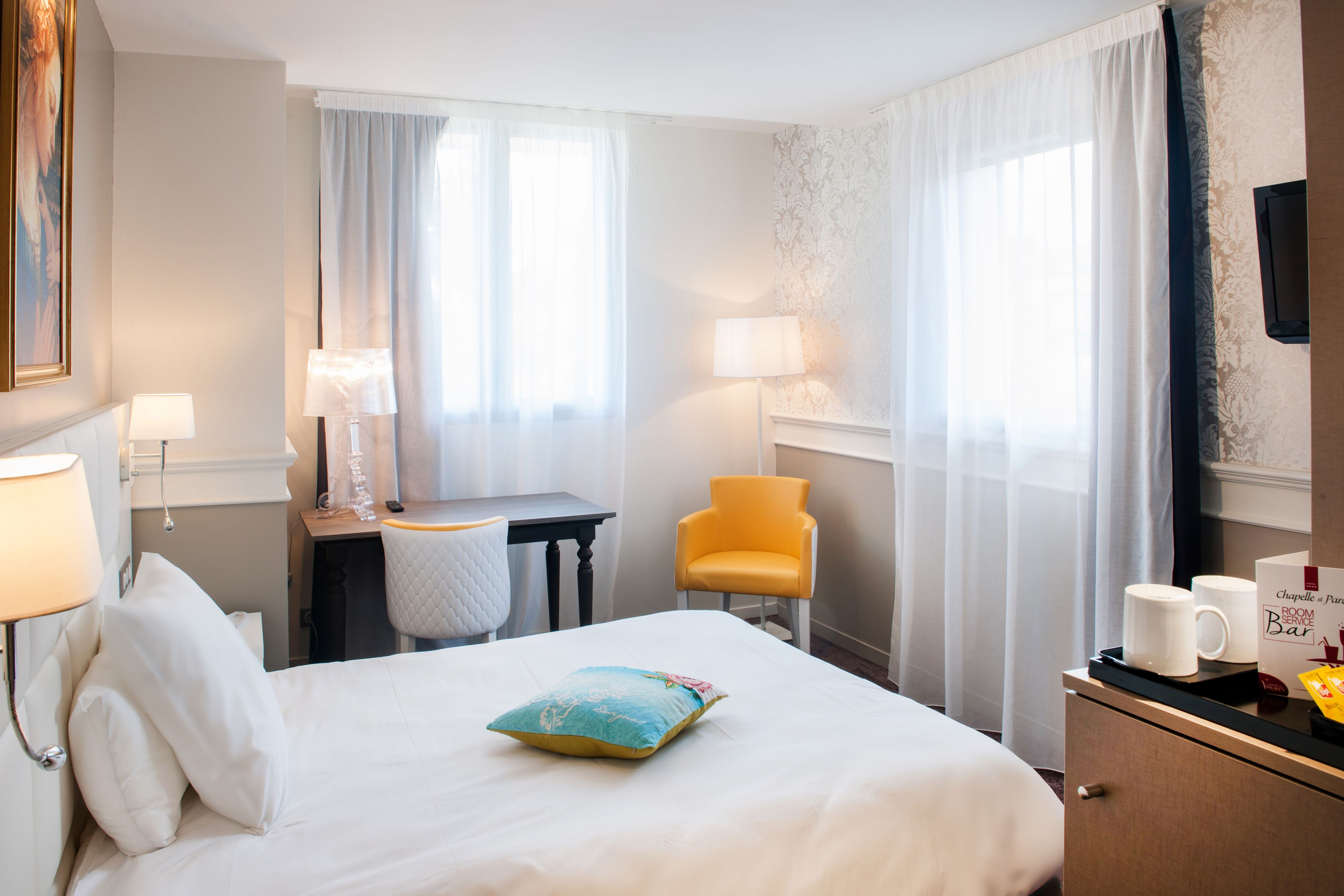 A hotel room with a bed, a desk, a chair, a TV, and a minibar.