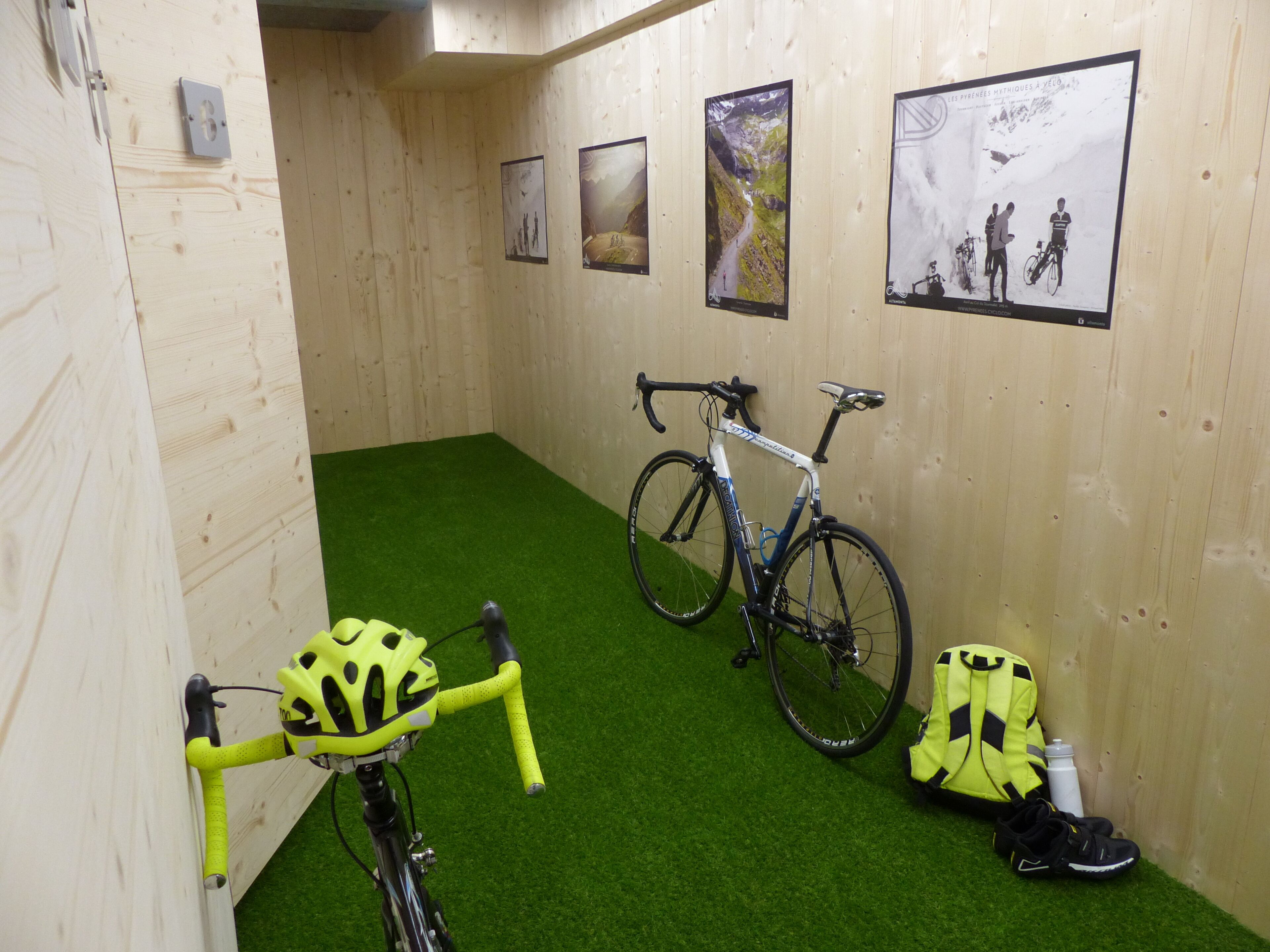 Una habitación con pared de madera, alfombra verde, una bicicleta, un casco y una mochila.